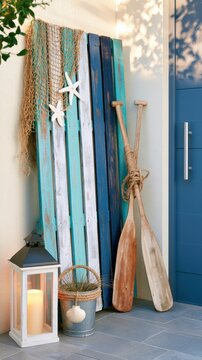 Coastal porch d&eacute;cor with distressed wooden pallet, vintage oars, fishing net, lantern, and seaside accents in warm natural light at a beach cottage entrance.