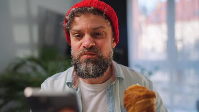 A man enjoying a fresh croissant for breakfast and using his smartphone