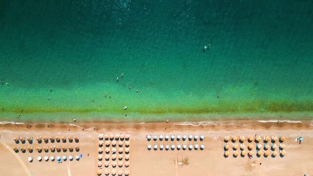 Top-down view of sandy beach with sun umbrellas and turquoise sea water