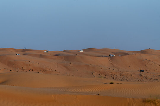 View of off-road vehicles driving across the vast orange sand dunes of the desert under a clear blue sky in Bidiyah, Ash Sharqiyah North G, Oman.