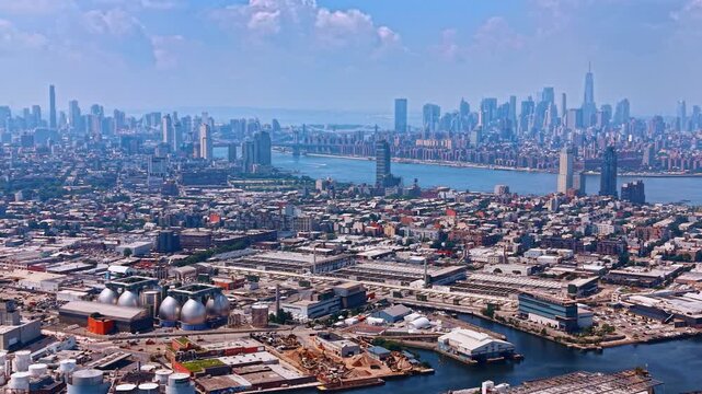 Flight over Brooklyn and Queens with storage tanks, scrap yards, manufacturing facilities, warehouses, and freight railways. New York City famous skyline in the backdrop.