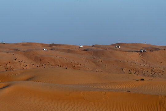 View of off-road vehicles driving across the vast orange sand dunes of the desert landscape in Bidiyah, Ash Sharqiyah North G, Oman.