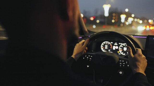 Backseat view on man driving car through the streets of the evening city.