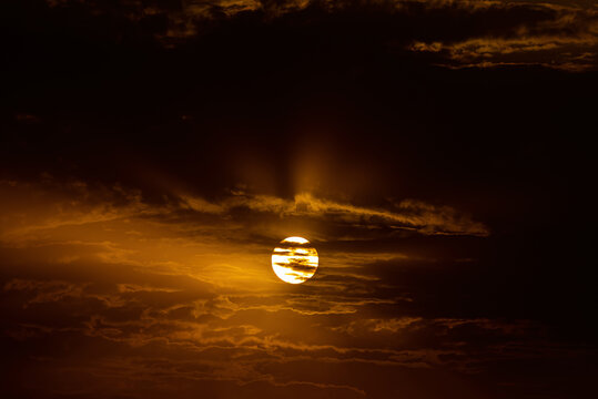 View of the sun setting behind dark clouds, casting a warm golden glow across the sky in Jahanian, Pakistan.