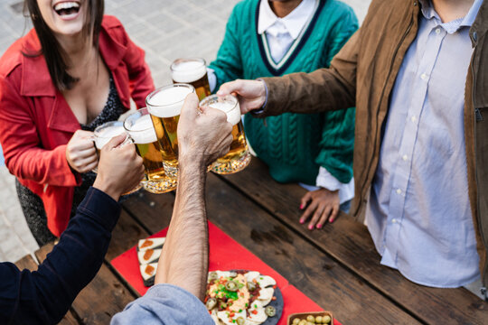 Young friends having fun together drinking craft beers at pub restaurant - Youth lifestyle and party concept - Focus on center hand holding glass