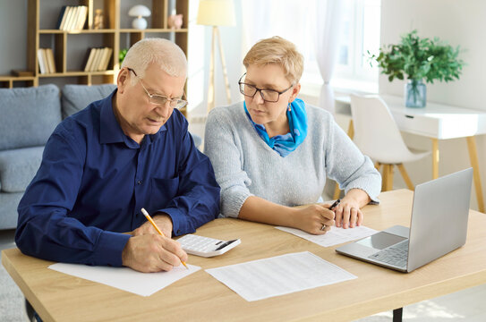 Seniors couple budgeting bills with calculator laptop. They review paperwork and verify payments for accurate finance and retirement planning. Concept of household budgeting and savings.