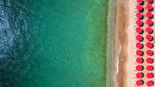 Top-down view of sandy beach with sun umbrellas and turquoise sea water