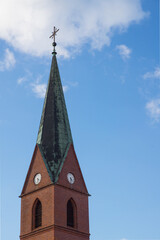 Fototapeta premium Historic Red Brick Church Tower with Clock and Spire Against Blue Sky