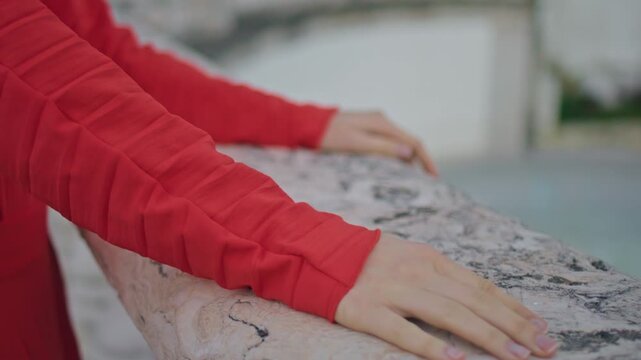 Female hands touching marble railing close up. Lady red dress stone parapet.