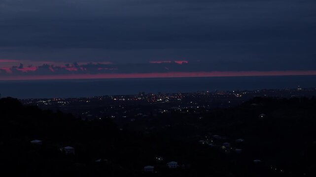 Dramatic transition from dusk offensive against the backdrop of coastal cityscape Kobuleti, Georgia, bright pink sunset disappears over sea, and city lights begin to twinkle illuminate dark landscape