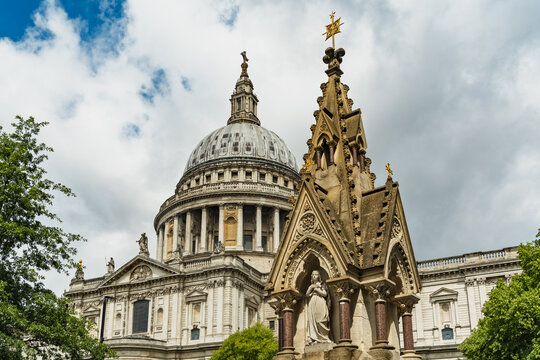 View of St. Paul's Cathedral with its iconic dome and a detailed stone monument in the foreground under a cloudy sky in London, England, United Kingdom.