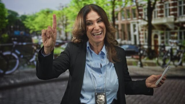 Woman points finger upward wearing police badge and holding notepad on a cobbled street; authority confidence.