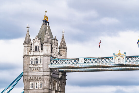 View of the iconic Tower Bridge with its ornate stone towers and blue steel suspension structure under a cloudy sky in London, England, United Kingdom.