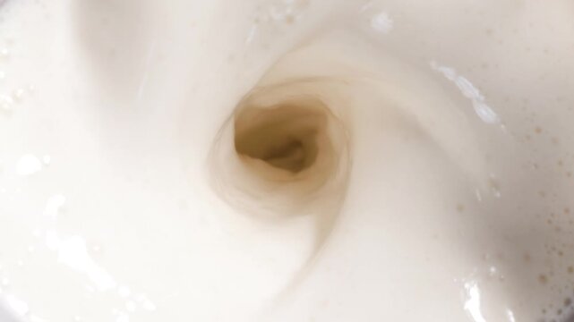 Creamy white milk swirling into a vortex inside blender jar, overhead macro of liquid motion