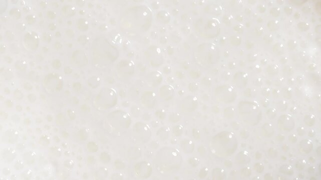 Creamy white froth and bubbles on blended milk drink surface, full-frame macro texture background