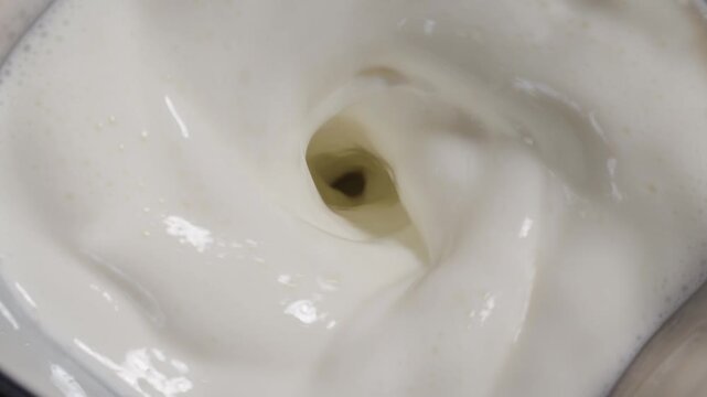 Creamy white milk swirling into a vortex inside blender jar, overhead macro of liquid motion