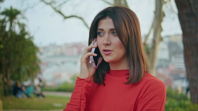 Brunette girl talking mobile phone city park. Close up female speaking outdoors.