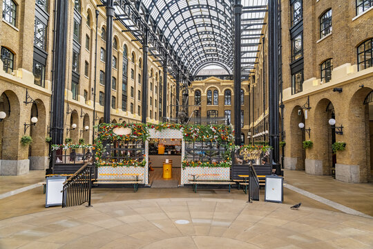 View of Hay's Galleria featuring its historic brick architecture, vaulted glass ceiling, and a floral-decorated kiosk London, England, United Kingdom.