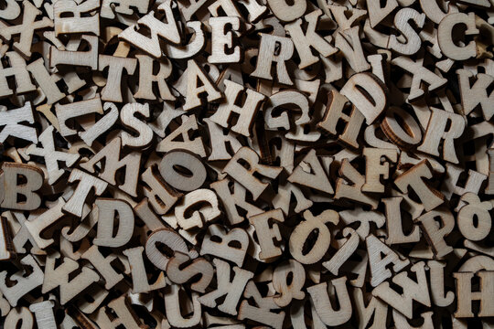 Top view full frame background of scattered small wooden alphabet letters creating messy jumbled texture for education and typography concepts, closeup