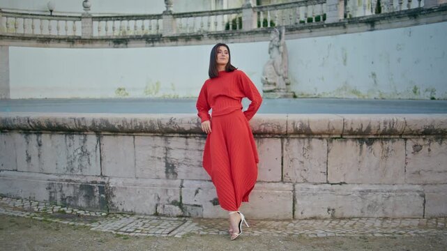 Fashion girl leaning stone fountain historic palace. Red outfit trendy look.