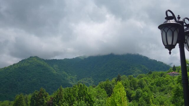 Dramatic gray clouds move rapidly over a lush green mountain mass covered in dense forest. With a lonely house visible among the bright trees in Georgia