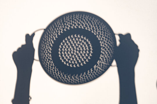 Person observing the partial solar eclipse in London, United Kingdom, using a  colander as a simple pinhole projection device during the August 12, 2026 astronomical event at 7:09 PM BST.