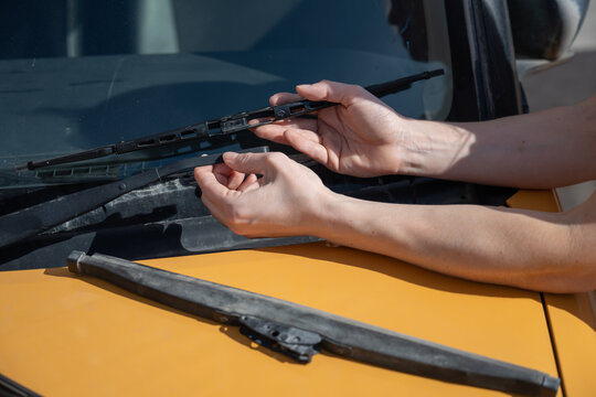A woman replaces old windshield wipers with new ones on a car.