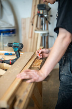 Preparation process in restoration workshop, man crafter working with wooden details and materials, craftsperson selecting and making marks on plank for window frame, handwork and reconstruction.