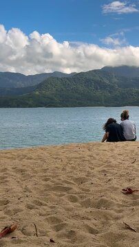 Mother and daughter enjoying family time at Feiticeira Beach in Ilhabela, with the beaches of S&atilde;o Sebasti&atilde;o in the background.