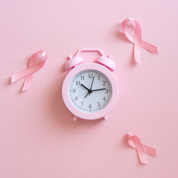 Breast cancer awareness month concept with pink alarm clock and ribbon on pastel square pink background