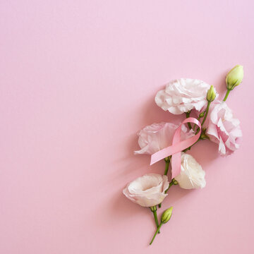 Breast cancer awareness month concept with pink ribbon and lisianthus flowers on square pastel pink background