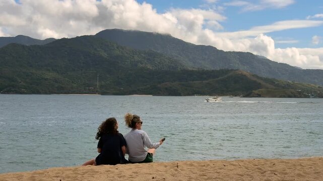 Mother and daughter enjoying family time at Feiticeira Beach in Ilhabela, with the beaches of S&atilde;o Sebasti&atilde;o in the background.