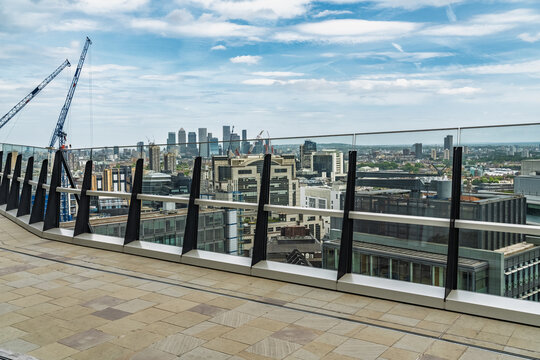 View of the London skyline featuring modern skyscrapers, construction cranes, and a glass balcony railing in the foreground under a blue sky in London, England, United Kingdom.