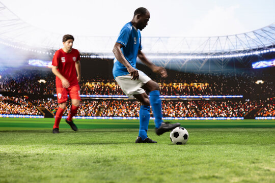 Blue soccer player controls and dribbles the ball in attack, using quick footwork to move past a red opponent during a dynamic one-on-one possession duel on the pitch in a competitive match.