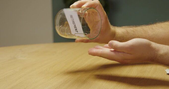 Person emptying coins from a glass jar labeled &ldquo;Retirement,&rdquo; representing retirement savings, pension planning, financial security and future expenses.
