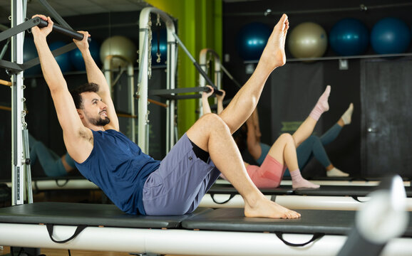 Fit young man performing V-sit movement for core stability on professional reformer equipment