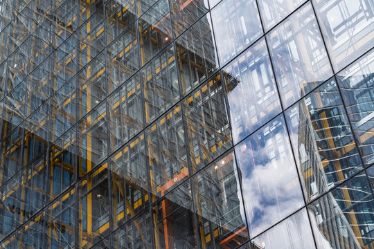 View of the modern glass facade of a skyscraper with yellow structural steel beams and reflections of clouds in London, England, United Kingdom.