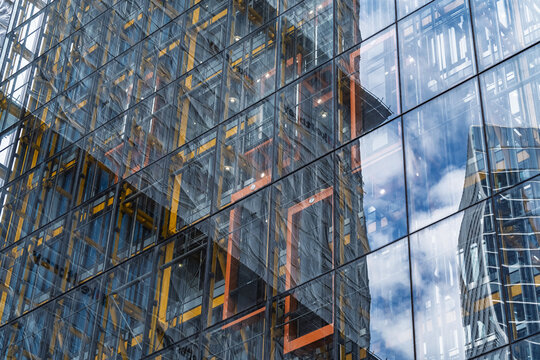 View of the glass facade and yellow steel structure of the Leadenhall Building reflecting the blue sky in London, England, United Kingdom.