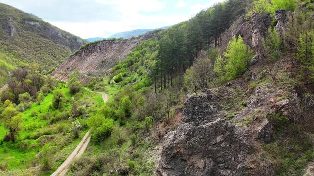 Aerial 4K Drone View of Dark Rugged Rocky Peak Rising Over Green Forest Valley in Bulgaria