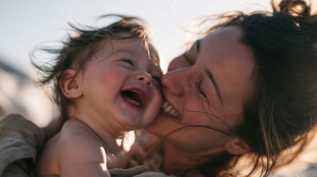 Happy Mother Hugging and Kissing Her Laughing Baby Outdoors