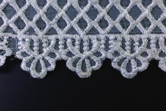 Blue and white patterned woven cotton fabric border showing a delicate white scalloped crochet lace trim edge isolated on a black background for graphic design composites