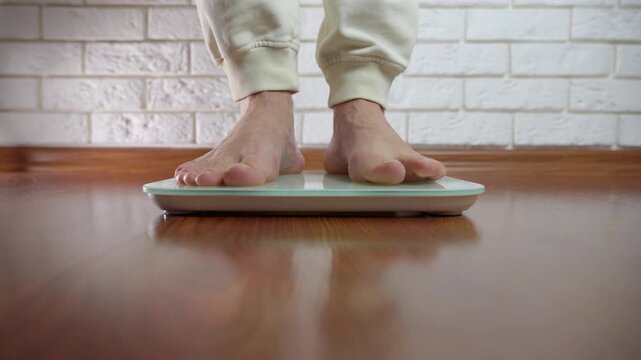 Person checking body weight on a smart digital scale at home. Low angle view of male bare feet stepping on a digital smart scale to measure body weight. Healthy lifestyle, diet, and weight loss