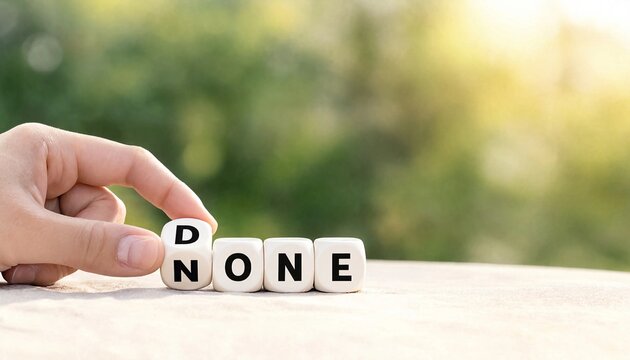 Hand turning wooden block changing the word none to done against blurred green background