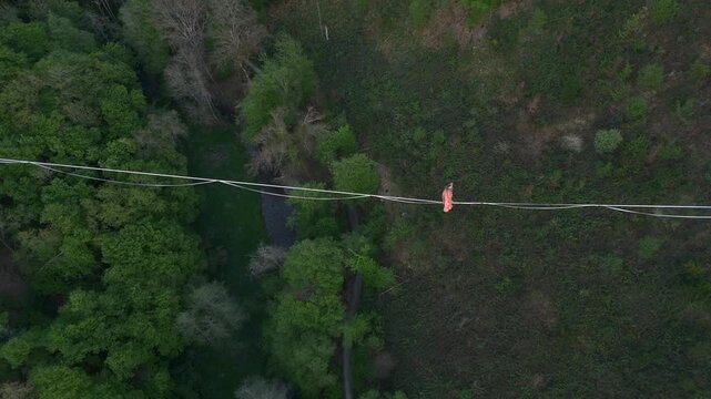 Highline Aerial Shot. Brave Girl Tightrope Walker is on a rope stretched between Mountains at high altitude, Sunset Time