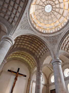 View of the interior of the Catedral de San Ildefonso featuring stone columns, a vaulted ceiling, and a wooden crucifix in Merida, Yucatan, Mexico.