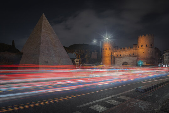 View of the Pyramid of Cestius and the historic Porta San Paolo illuminated at night with vibrant light trails from passing traffic in Rome, Lazio, Italy.
