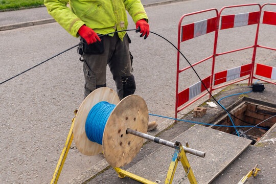 Engineer feeding fibre cable from drum into chamber at street works