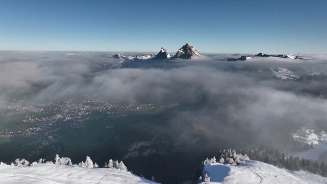 Aerial Drone View of Swiss Alpine Peaks Rising Above Cloud Sea with Snow Covered Forest Below