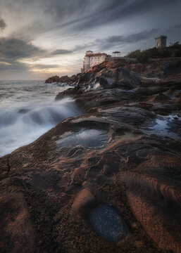 View of Castello del Boccale overlooking the rocky coastline and sea waves during sunset in Calafuria, Toscana, Italy.