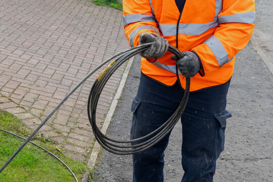 Engineer coiling black fibre optic cable by hand at street works